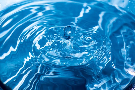 Water drops on blue surface. Water ripple background. Splashes from a drop of water. Raindrops on a blue background. The texture of the water. Aqua, turquoise, macro