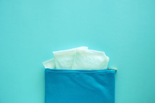 Sanitary napkin in women's fabric bag on blue background for hygiene and health concept