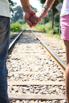 Rear view of loving couple holding hands and walking together at railroad tracks for travel, love and Valentine's day concept