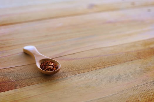 A spoon of cayenne pepper on wooden background for food ingredients and cooking concept