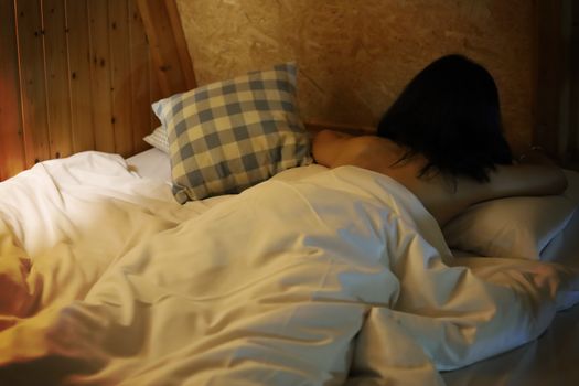 Rear view of a naked woman lying down on the bed at night with dark tone image