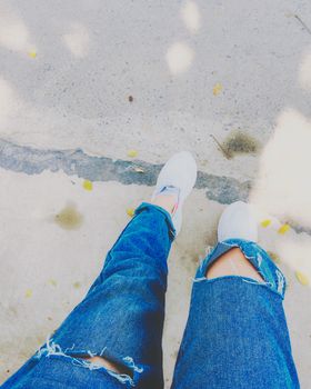 Woman's legs with blue fashion jeans and white sneakers on street for travel concept