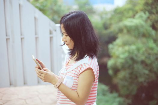 Young asian woman in casual clothes using smartphone and standing on the balcony for communication and technology concept