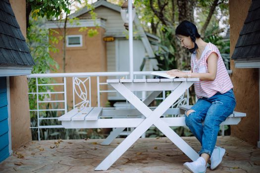 Young asian girl sitting on the white wooden table and reading a book at the terraces for relaxation