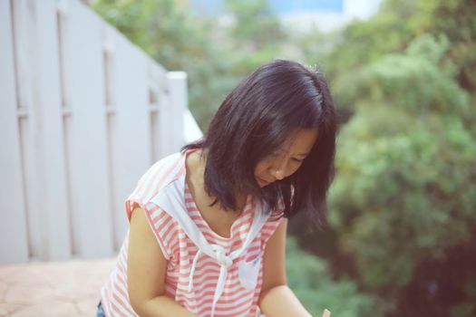 Young asian woman in casual clothes standing alone and looking down on the balcony against burred green natural background