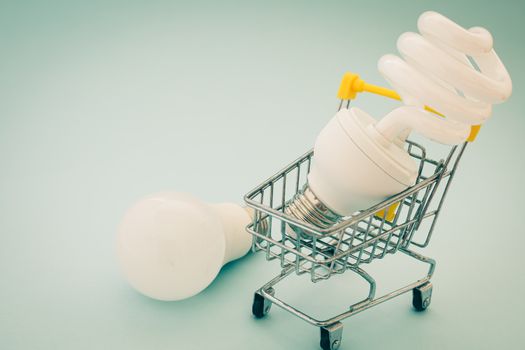 Fluorescent and LED light bulb with mini shopping cart or trolley on blue background for energy savings concept