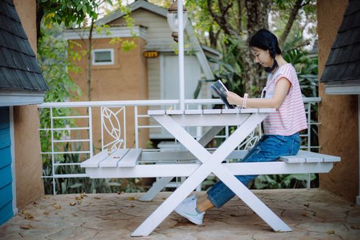 Young asian girl sitting on the white wooden table and reading a book at the terraces for relaxation