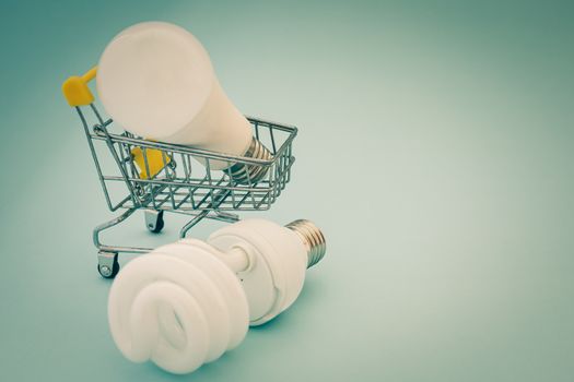 Fluorescent and LED light bulb with mini shopping cart or trolley on blue background for energy savings concept