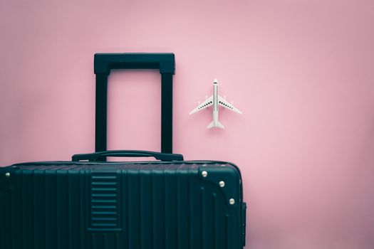 Black luggage and white airplane model on pink background for travel and journey concept
