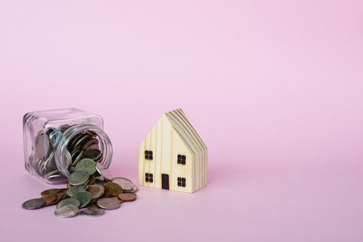 Wooden house model with money coins in the glass jar on pink background with copy space for business and finance for property concept