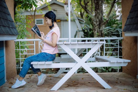 Young asian girl sitting on the white wooden table and reading a book at the terraces for relaxation