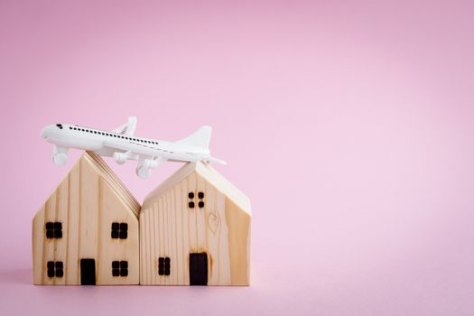 White airplane and wooden house model on pink background for travel concept