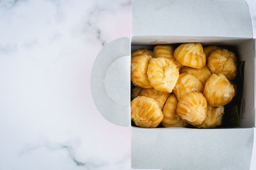 Delicious eclair vanilla cream, choux dough filled with a cream, homemade bakery in paper box packaging on white marble background for snack eating concept