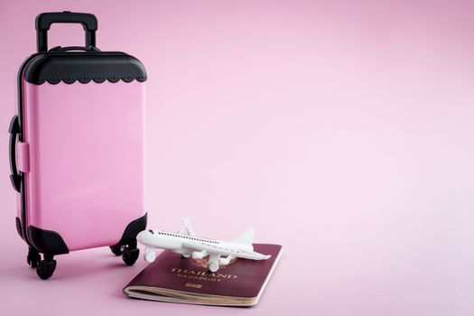 Pinky luggage with Thai passport and white airplane model on pink background for travel and journey concept