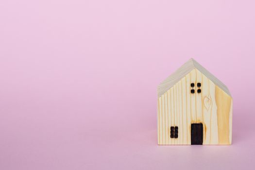 Wooden house model on pink background with copy space for housing concept