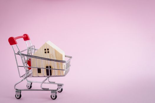 Wooden house model in the shopping cart on pink background for housing and property concept