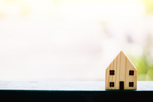 Wooden house model against blurred natural outdoor background with copy space for housing concept