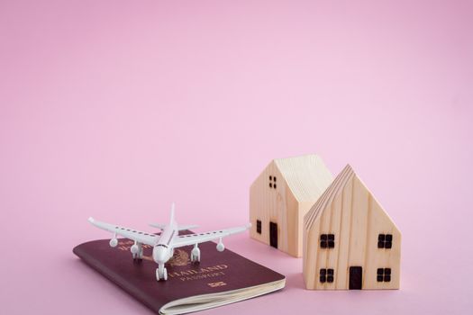 White airplane, Thai passport and wooden house model on pink background for travel concept
