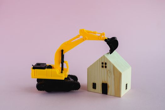 Wooden houses with excavator loader model on pink background for housing and construction concept