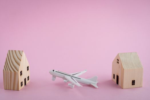 White airplane and wooden house model on pink background for travel concept