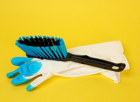 rubber glove and black plastic brush for cleaning the house on a yellow background, close up