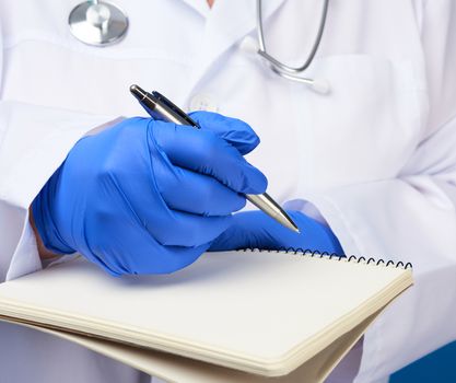 medic woman in white coat, blue latex gloves holding an open notebook with white sheets, blue background, close up