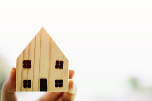 Hand holding wooden house model against blurred natural outdoor background with copy space for housing concept