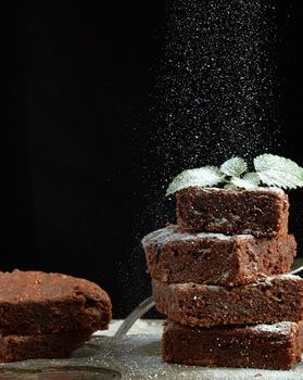 stack of square baked brownie chocolate cake slices sprinkled with white sugar, small particles fly down, low key