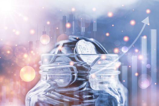 Coins in the glass jar against blurred natural background with growing graph and light effect for save money, business and finance concept