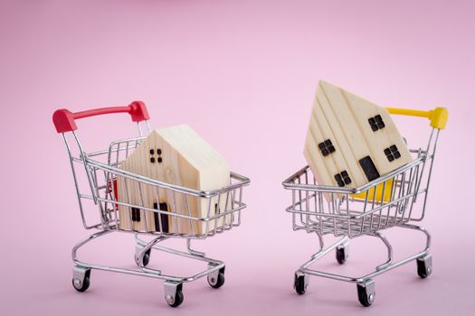 Wooden house model in the shopping cart on pink background for housing and property concept