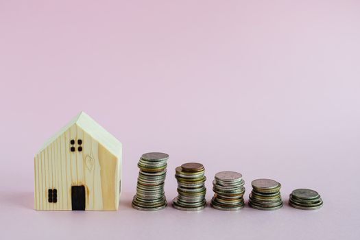 Wooden house model with step of money coins on pink background with copy space for business and finance for property concept
