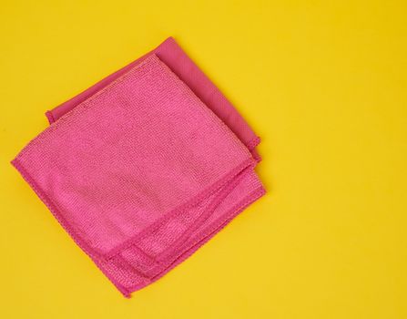 folded pink rags for cleaning on a yellow background, top view