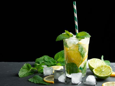 summer refreshing drink lemonade with lemons, mint leaves, ice cubes and lime in a glass on a black background,  copy space