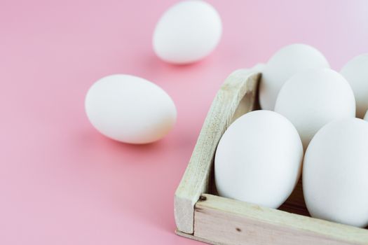 White eggs in the wooden tray on pink background for healthy food concept