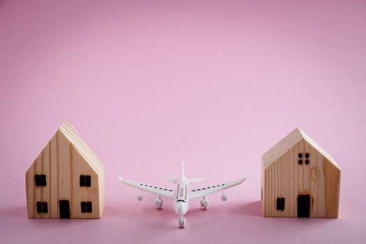 White airplane and wooden house model on pink background for travel concept
