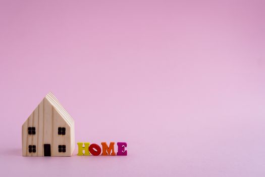 Wooden house model with HOME alphabet on pink background for housing concept