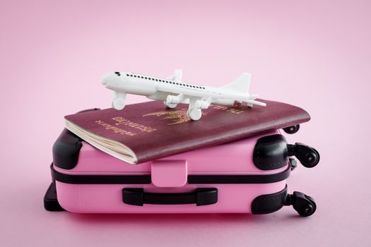 Pinky luggage with Thai passport and white airplane model on pink background for travel and journey concept
