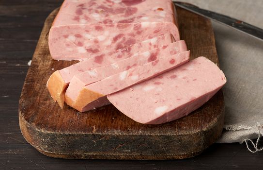 sliced boiled sausage with slices of whole meat on a brown wooden cutting board, close up