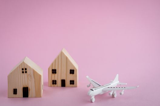 White airplane and wooden house model on pink background for travel concept