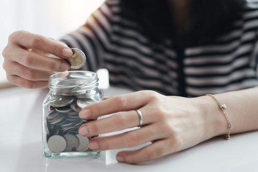 Woman's hand saving a coin into the glass jar for planning, business and finance concept