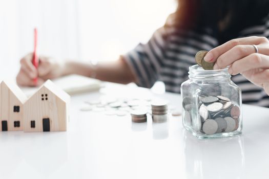 Woman's hand saving a coin into the glass jar for planning, housing and property financial concept