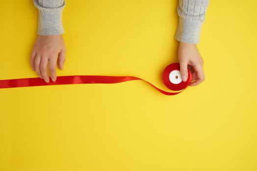two female hands and red ribbon on a yellow background, top view