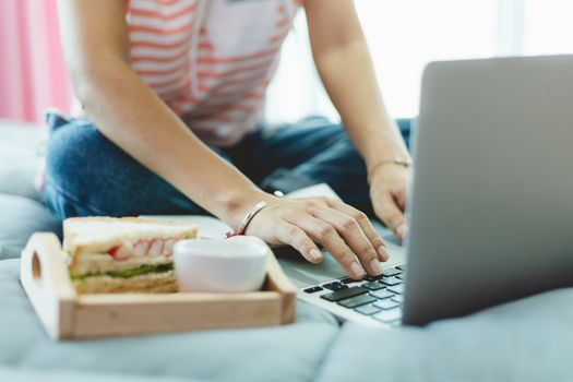 Woman using computer and having breakfast in bed for self-quarantine, social distancing, staying and working at home in coronavirus or Covid-2019 outbreak situation concept