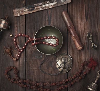 Copper singing bowl, prayer beads, prayer drum and other Tibetan religious objects for meditation and alternative medicine on a brown wooden background