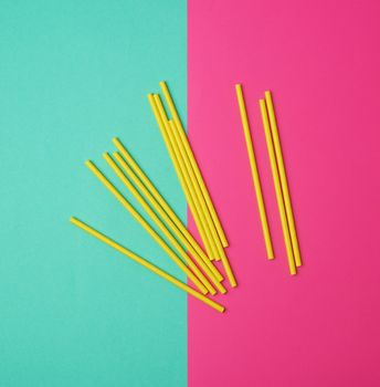 stack of yellow paper tubes for a cocktail on a multi-colored background, concept of rejection of plastic and the use of recyclable materials