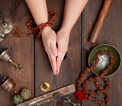 two hands in a prayer pose on a wooden brown table in the middle of vintage Tibetan meditation tools, alternative medicine, top view