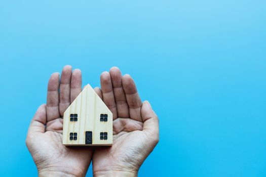 Hand holding wooden house model on blue background for self-quarantine, staying home and social distancing in coronavirus or Covid-2019 situation concept