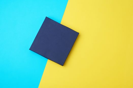 closed dark blue paper cardboard box on a yellow-blue background, concept of surprise, top view