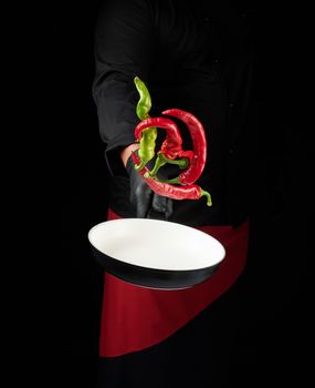 chef in black uniform and red apron holds a round pan with fresh chili peppers, low key