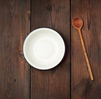 empty round metal white plate and wooden spoon on the table, top view